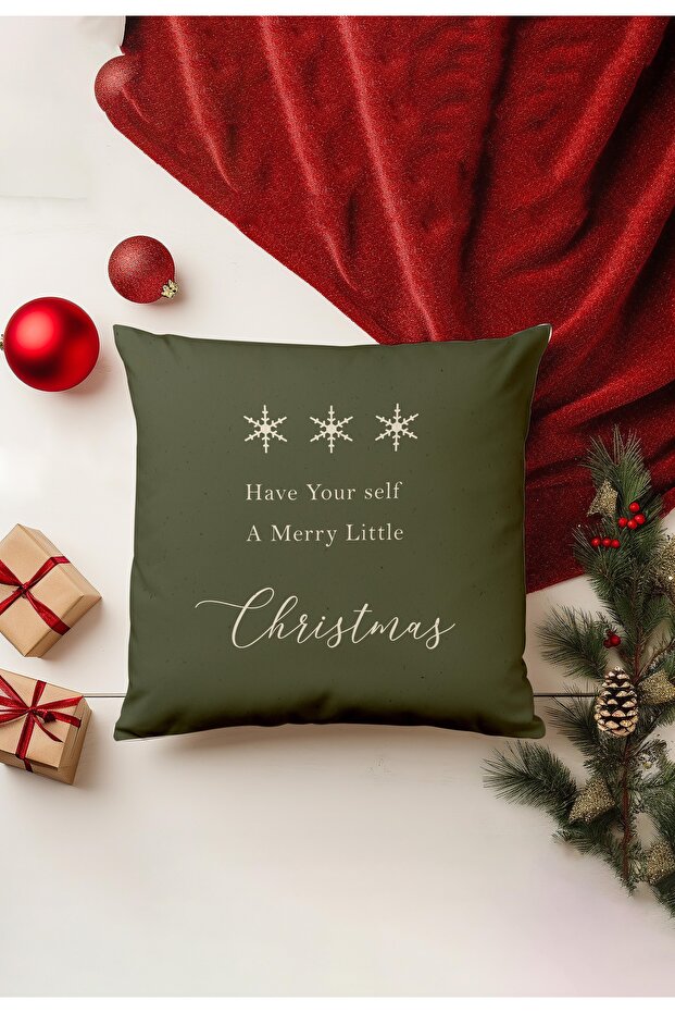 Green pillow with Christmas message on a festive background with red decorations and tree.