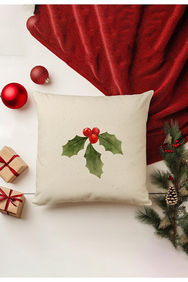 Decorative pillow with holly design on a white surface with Christmas decorations.